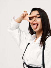 brunette in a white shirt holds two fingers in front of her eyes and smiles