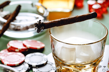 Glass of whiskey, cigar, playing cards and chips on green background