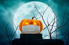 Halloween Jack O Lantern Pumpkin Wearing Medical Face Mask On The Rock Over Dead Tree, Moon And Cloudy Spooky Sky, Halloween And Coronavirus Or Covid-19 Concept