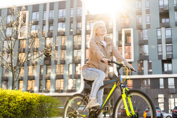 Wall Mural - Happy smiling woman cheerfully spreads legs on bicycle on the country road under blossom trees. Spring is comming concept image.