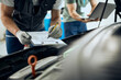 © Drazen - Close-up of mechanic writing data while examining car engine in a workshop.