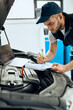 Auto mechanic writing notes while running car diagnostic and examining engine at repair shop.