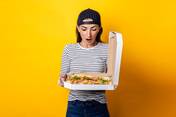 young woman pizza delivery man looking in surprise at holding pizza on yellow background