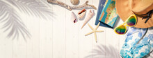 白いウッドデッキの上にある麦わら帽子、サングラス、ビーチサンダルなど夏のリゾートのイメージ。もしくは海外旅行のイメージ。真上からのアングル