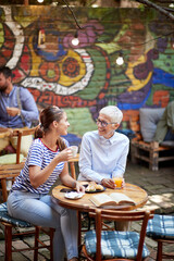 Wall Mural - Two happy female friends of different generations chatting while they have a drink in the bar. Leisure, bar, friendship, outdoor