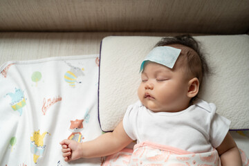 asian baby infant get fever and apply cool patch on forehead sleeping at home after vaccination. col