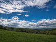 Blick in die Weite des Odenwalds über Felder, Wiesen und mit einem schon dreidimensionalen blauen Himmel mit weißen Wolken im Frühling
