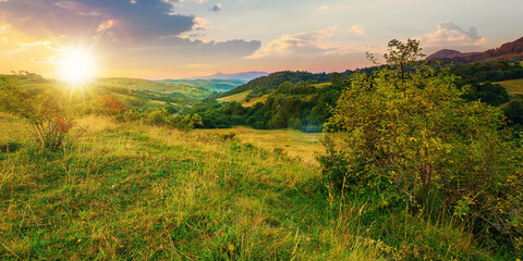 mountainous rural landscape at sunset. beautiful scenery with forests, hills and meadows in evening light. ridge with high peak in the distance. village in the distant valley