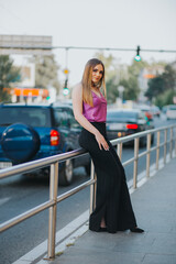 Wall Mural - Gorgeous Caucasian female in stylish purple and black outfit leaning on a street fence