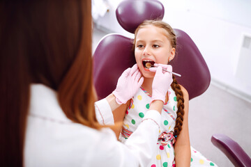 Little girl visiting dentists. Pretty girl opening his mouth wide during treating her teeth by the dentist.  Early prevention, oral hygiene and milk teeth care.