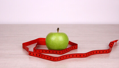 Green apple and red measuring tape. The concept of a healthy diet. Diet for health and a good figure