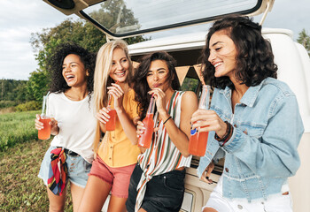 Wall Mural - Group of four female friends celebrating during road trip standing at minivan