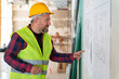 © bulentbaris - Builder in working uniform with protective helmet standing with instruments at the construction site indoors