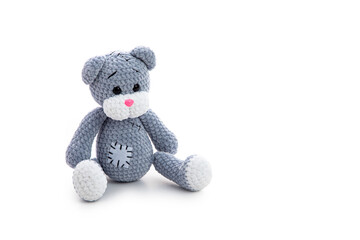 grey knitted teddy bear toy with patch sitting over white background with soft shadow