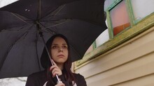 Close Up Of Sad Woman With Umbrella Standing Near House. Portrait Of Thoughtful Female Looking Away And Standing On Street In Rain.