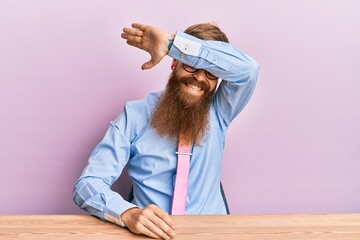 Canvas Print - Young irish redhead man wearing business shirt and tie sitting on the table covering eyes with arm smiling cheerful and funny. blind concept.