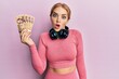 © Krakenimages.com - Beautiful blonde caucasian woman wearing gym clothes holding hungarian forints scared and amazed with open mouth for surprise, disbelief face