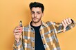 Young hispanic man holding electronic cigarette with angry face, negative sign showing dislike with thumbs down, rejection concept