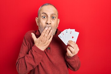 Canvas Print - Handsome mature man playing poker holding cards covering mouth with hand, shocked and afraid for mistake. surprised expression