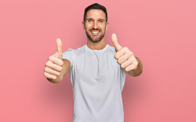 Canvas Print - Handsome man with beard wearing casual white t shirt approving doing positive gesture with hand, thumbs up smiling and happy for success. winner gesture.