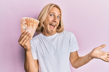 Sticker - Caucasian young man with long hair holding 20 philippine peso banknotes celebrating achievement with happy smile and winner expression with raised hand