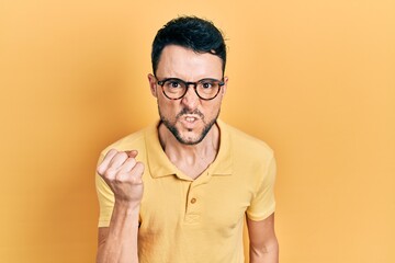 Poster - Young hispanic man wearing casual clothes and glasses angry and mad raising fist frustrated and furious while shouting with anger. rage and aggressive concept.