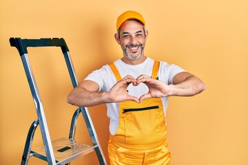 Poster - Handsome middle age man with grey hair holding ladder smiling in love doing heart symbol shape with hands. romantic concept.