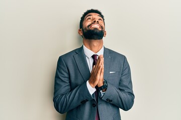 Canvas Print - Handsome hispanic man with beard wearing business suit and tie begging and praying with hands together with hope expression on face very emotional and worried. begging.