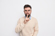 Serious bearded man makes silence gesture prohibits to speak shows hush sign has strict face expression wears casual clothes isolated over white background asksto keep voice down scolds bad behavior