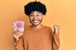 © Krakenimages.com - Young african american man with afro hair holding 100000 indonesian rupiah screaming proud, celebrating victory and success very excited with raised arm