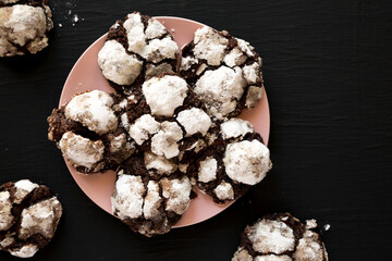 Wall Mural - Homemade Chocolate Crinkle Cookies on a pink plate on a black surface, top view. Overhead, from above, flat lay. Space for text.