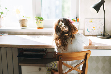 Little child beautiful girl with long hair in home clothes painting at desk in children room at the home