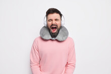 Exhausted Bearded Man Passenger Yawns With Wide Opened Mouth Keeps Eyes Closed Listens Music Via Headphones While Traveling By Car Or Plane Dressed In Casual Sweater Isolated Over White Background