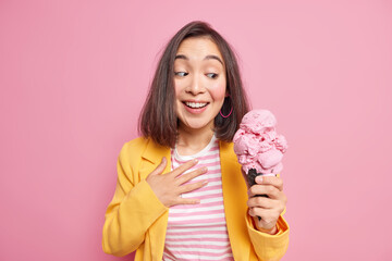 Wall Mural - Photo of good looking young Asian woman with dark hair holds yummy ice cream in waffle cone smiles gladfully dressed in stylish outfit wants to eat delicious frozen summer dessert. Enjoy it.