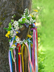 Spring flower wreath with colorful ribbons in garden. floral traditional decor. Symbol of Beltane, Wiccan Celtic Holiday beginning of summer. wheel of the year, pagan witch traditions and rituals