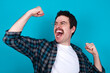 © Jihan - Attractive young Caucasian man with moustache wearing plaid shirt against blue wall celebrating a victory punching the air with his fists and a beaming toothy smile