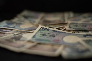 Blurred focus of pile of Japanese money in 1000 yen bills and 10000 yen bills on black background in soft focus