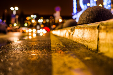 Rainy night in the parking shopping mall, the headlights of the approaching cars. Close up view of a level curb on the road