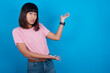 Young beautiful asian girl wearing pink t-shirt against blue background pointing aside with both hands showing something strange and saying: I don't know what is this. Advertisement concept.