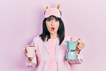 Poster - Young hispanic woman wearing sleep mask and robe drinking coffee afraid and shocked with surprise and amazed expression, fear and excited face.