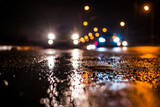 Fototapeta Natura - Rainy night in the big city, the cars traveling towards the headlights illuminate the road. Close up view from the level of the dividing line