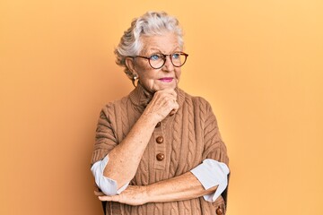 Senior grey-haired woman wearing casual clothes and glasses with hand on chin thinking about question, pensive expression. smiling with thoughtful face. doubt concept.