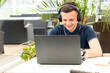 © A Stock Studio - Young man watches a webinar and listens to headphones while sitting at a table in a co working cafe. A male freelancer works at a laptop and listens to music.