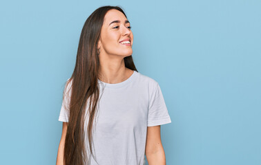 Young hispanic girl wearing casual white t shirt looking away to side with smile on face, natural expression. laughing confident.