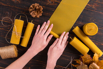 Women's hands make handmade candles of natural wax with texture of honeycomb bees, on a wooden table.