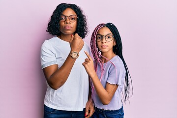 Canvas Print - Beautiful african american mother and daughter wearing casual clothes and glasses in hurry pointing to watch time, impatience, looking at the camera with relaxed expression