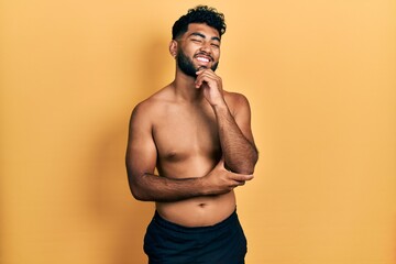 Canvas Print - Arab man with beard wearing swimwear shirtless looking confident at the camera with smile with crossed arms and hand raised on chin. thinking positive.