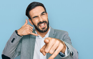 Young hispanic man wearing business clothes smiling doing talking on the telephone gesture and pointing to you. call me.