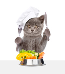 Poster - Kitten wearing chef's hat eats vegetables with knife and fork. isolated on white background