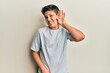 © Krakenimages.com - Teenager hispanic boy wearing casual grey t shirt smiling with hand over ear listening an hearing to rumor or gossip. deafness concept.